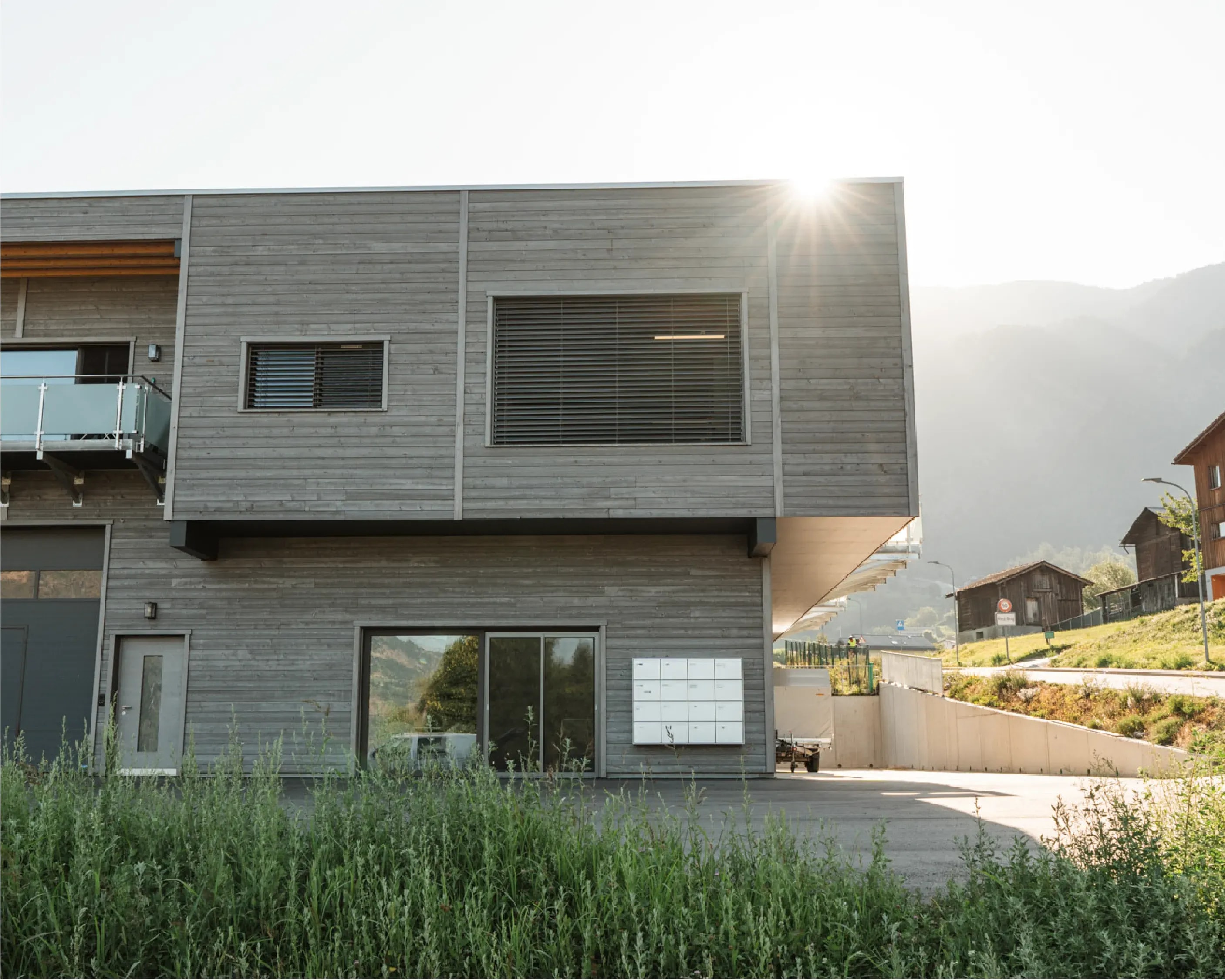 Moderner Gewerbebau mit grauer Holzfassade und auskragendem Obergeschoss im Gegenlicht, realisiert von der Holzbau AG.