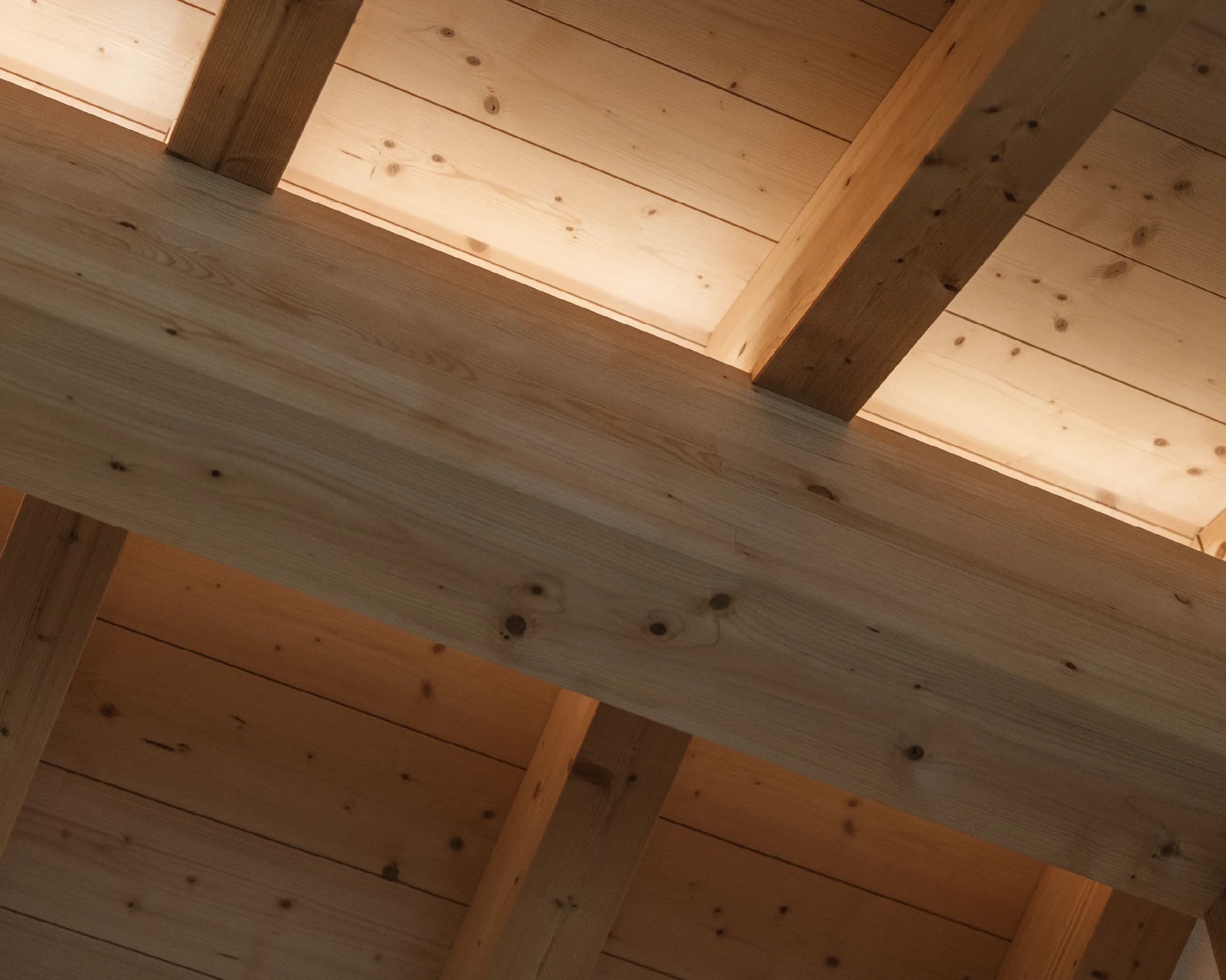 Detailaufnahme einer sichtbaren Holzbalkendecke aus hellem Fichtenholz mit warmem Streiflicht.