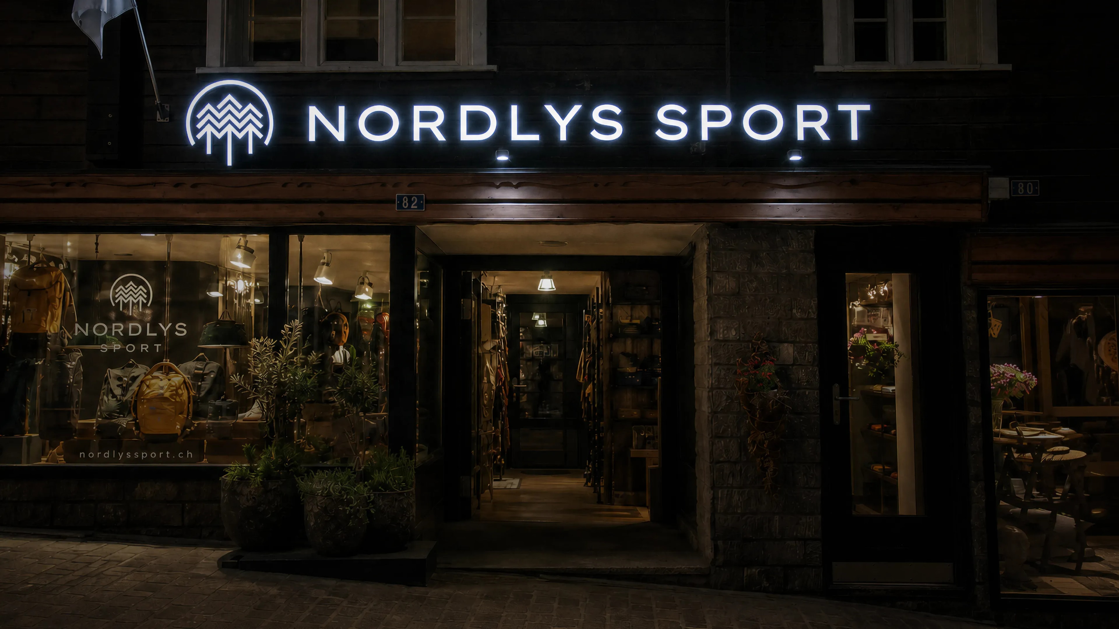 Ladenfront von Nordlys Sport in Leukerbad bei Nacht mit leuchtendem Schriftzug über dem Eingang und beleuchtetem Schaufenster.