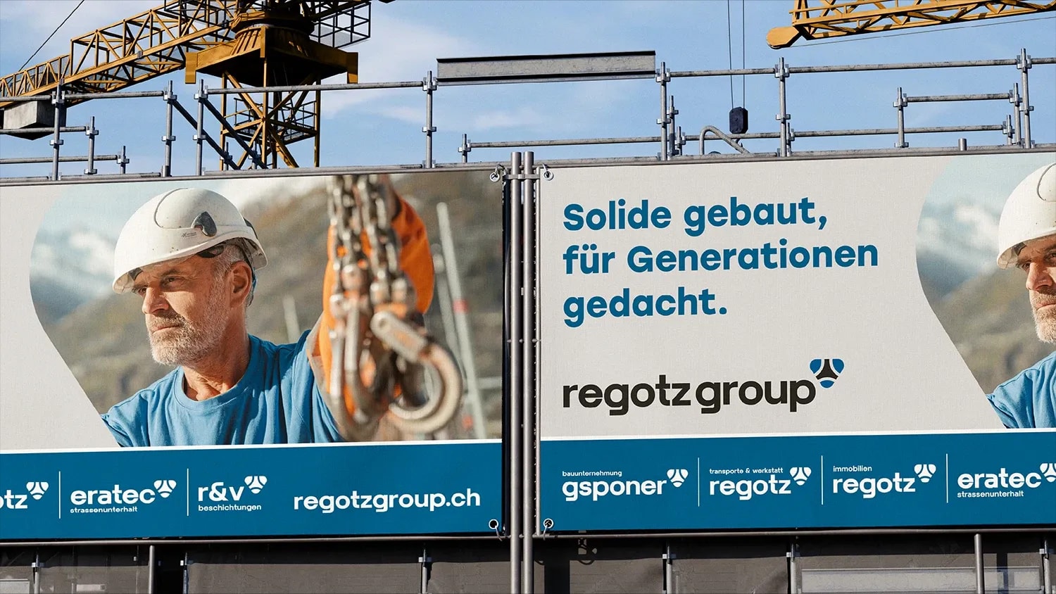 Bauwand mit Werbebanner der Regotz Group: Bauarbeiter am Kranhaken, Claim ‚Solide gebaut, für Generationen gedacht.' und die Logos der Gruppenfirmen.