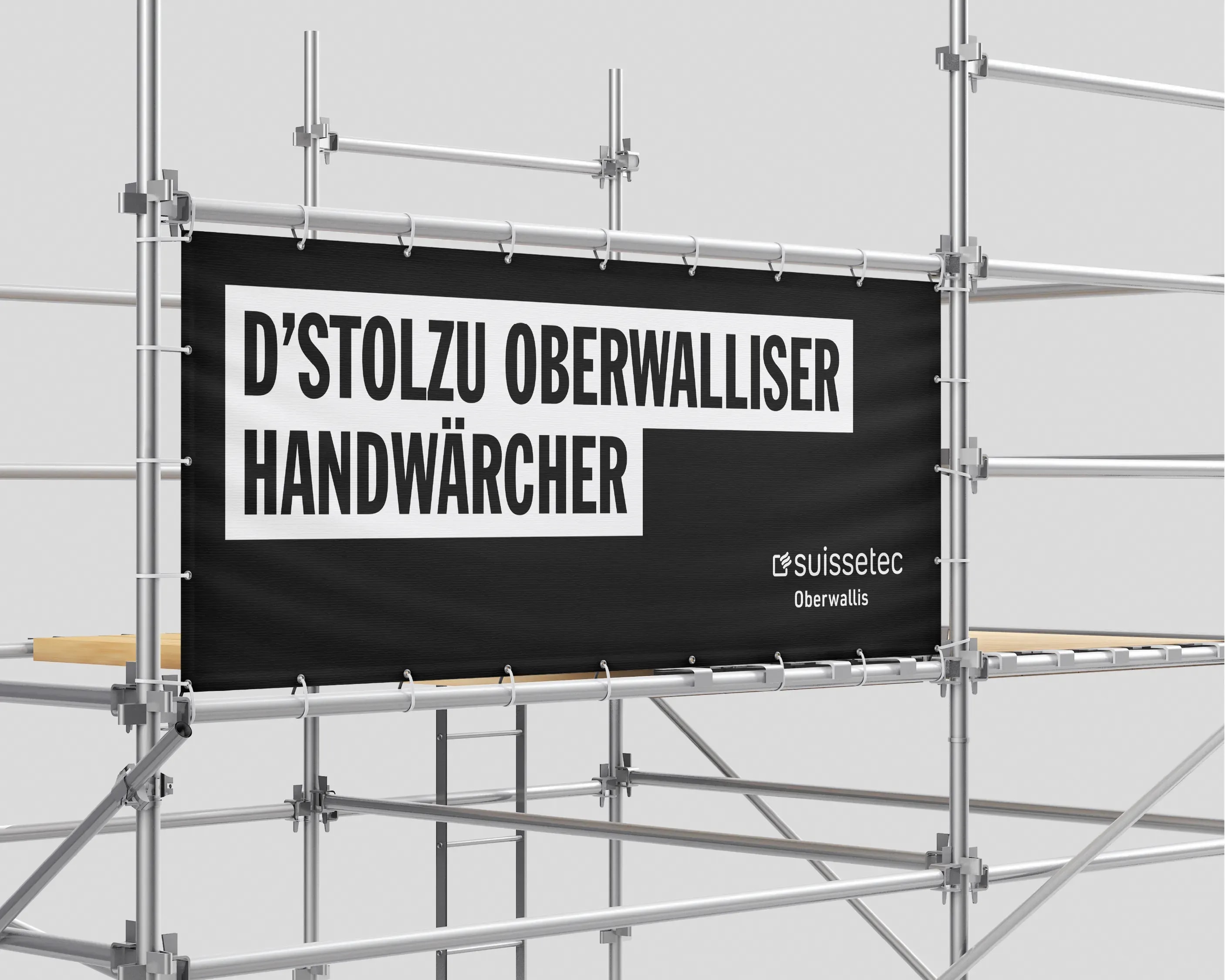 Schwarzes Banner mit dem Kampagnenclaim und dem Logo von suissetec Oberwallis, gespannt an einem Baugerüst.